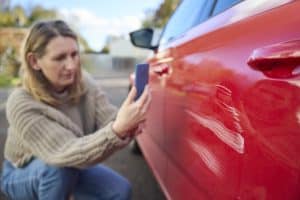 A female driver taking a picture of a scratch on her red car